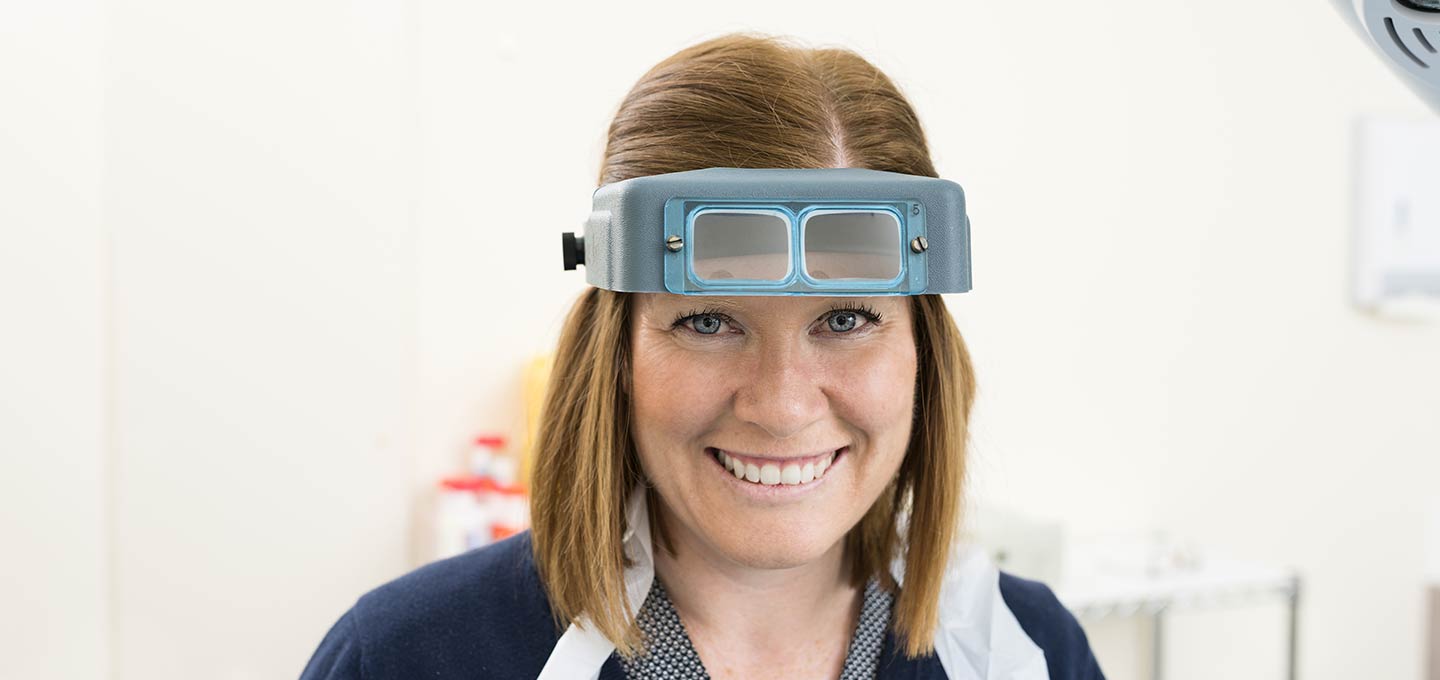A practice nurse smiling, wearing magnifying loupes